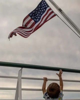 child reaching toward american flag on boat